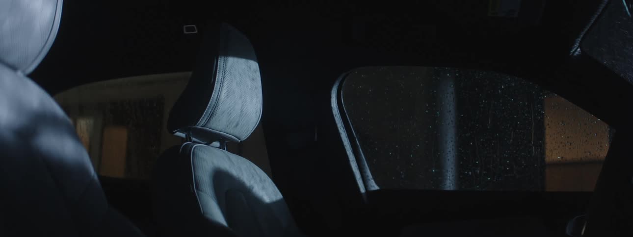 Rain falls on a car parked outside of a house