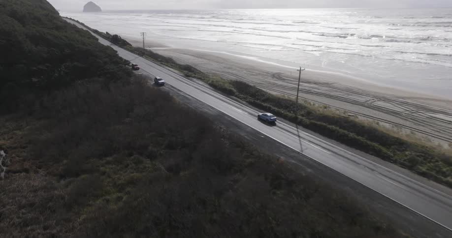 Aerial scenery of a car traveling along a road next to a beach and next to mountains during the day