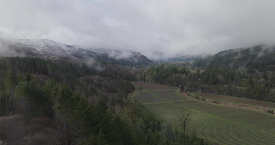 Aerial view of a field in a valley between mountains covered in clouds