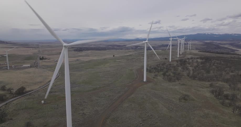 Aerial panorama of wind energy engines moving across fields and mountains