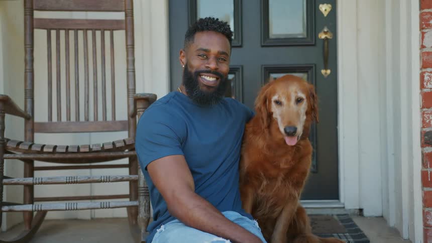 A man poses with his dog on the porch