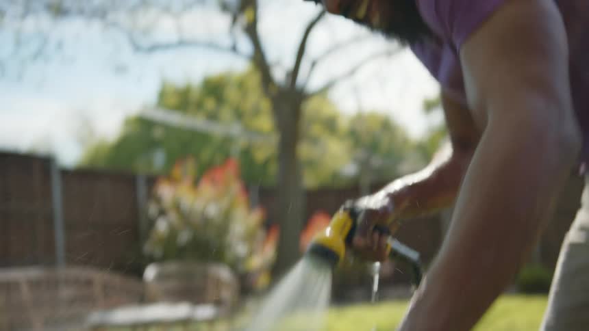 Smiling man bathing his dog with hose that swings and sprays water