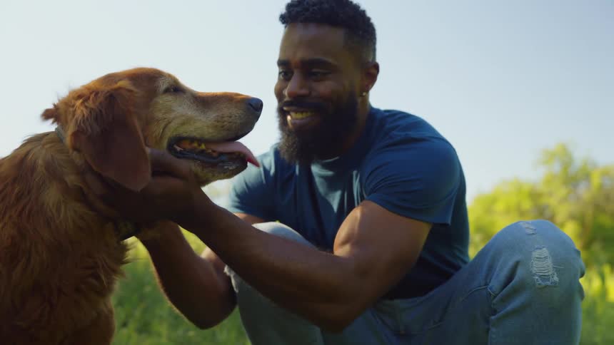 A smiling man is crouching and stroking his goldenhaired dog