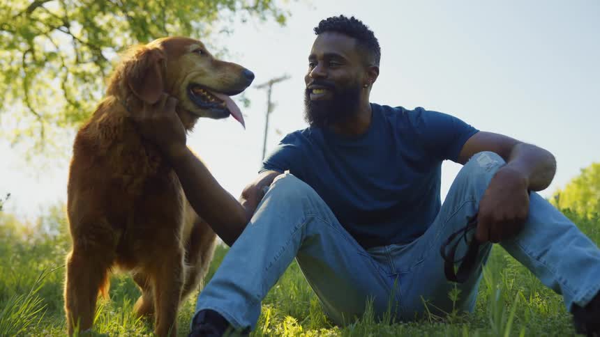 Man sitting on the grass in a park next to his golden retriever dog