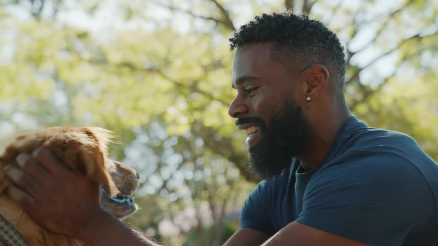 Man crouching down stroking his golden retriever dogs head