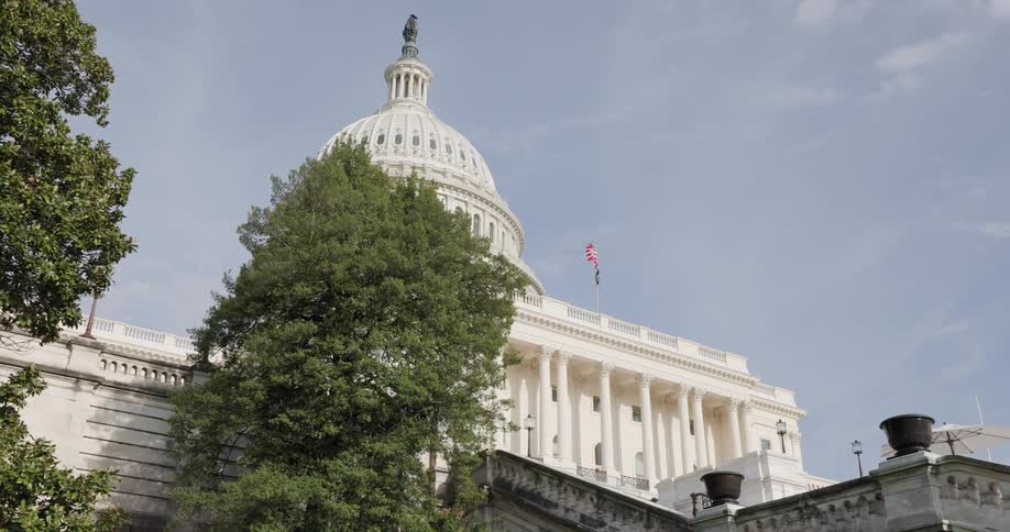 United states capitol on a blue sky day with trees around and an american flag on top