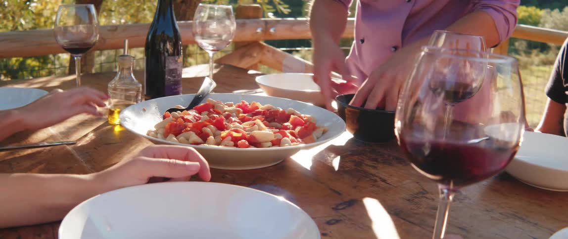 A person serves a plate of gnocchi on a table set for an outdoor meal