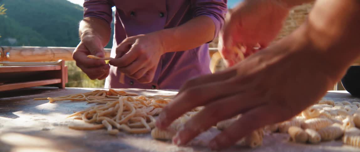 Two people prepare pasta outdoors