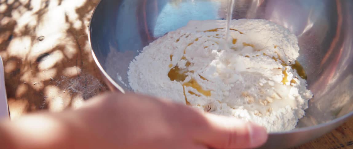 A chef is pouring water in a bowl of flour