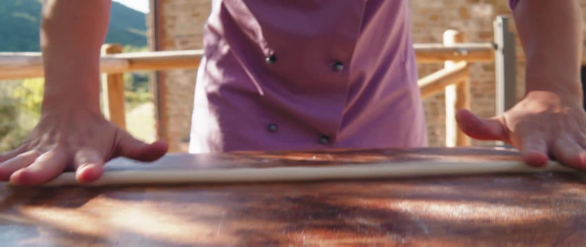 A womans hands working dough on a wooden surface and using a blue cutter to divide it into small pieces