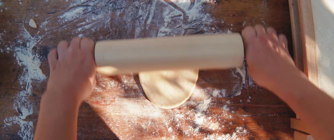Hands of a person preparing bread dough with a rolling pin
