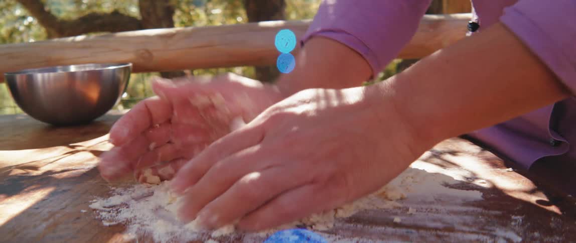 A restaurant worker kneads dough on an outdoor table