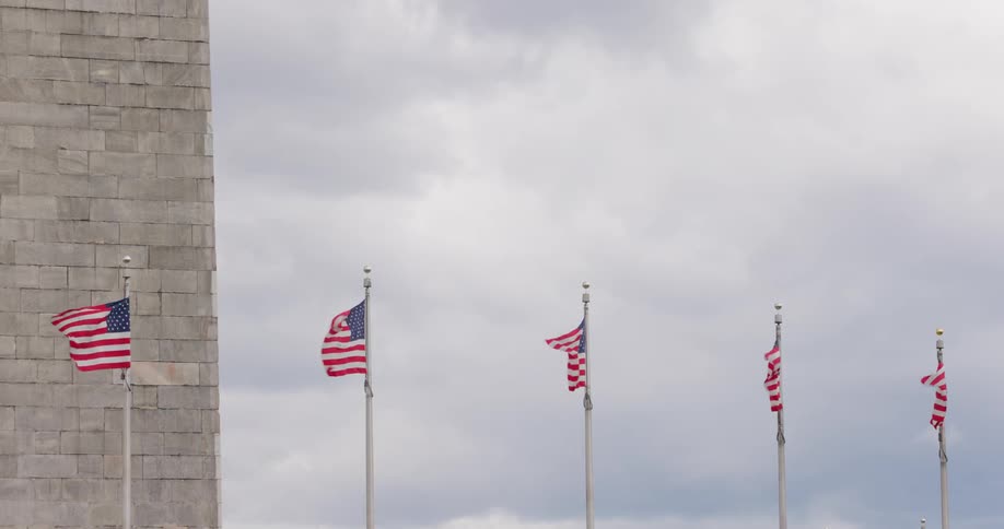 United states flags around a monument on a cloudy day