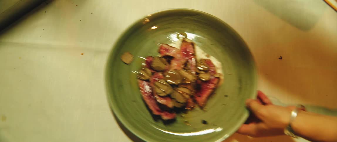A plate with sliced steak and truffle shavings on a table