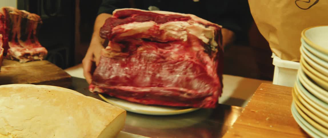 A man in a restaurant plates an enormous piece of raw meat