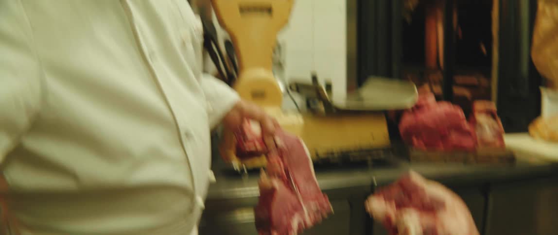 A butcher chops steak off a piece of meat