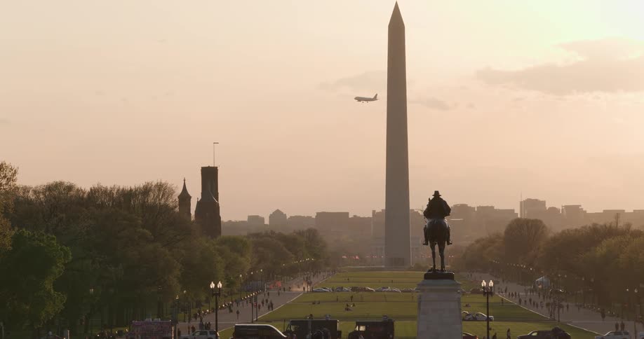 Panorama of the washington monument with the us capitol in the background and an equestrian statue in the foreground under an orange sky and the silhouette of a metropolis in the background