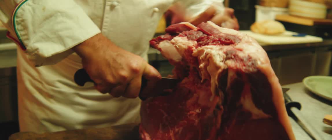 Hand of a chef using a knife and cutting a large piece of meat