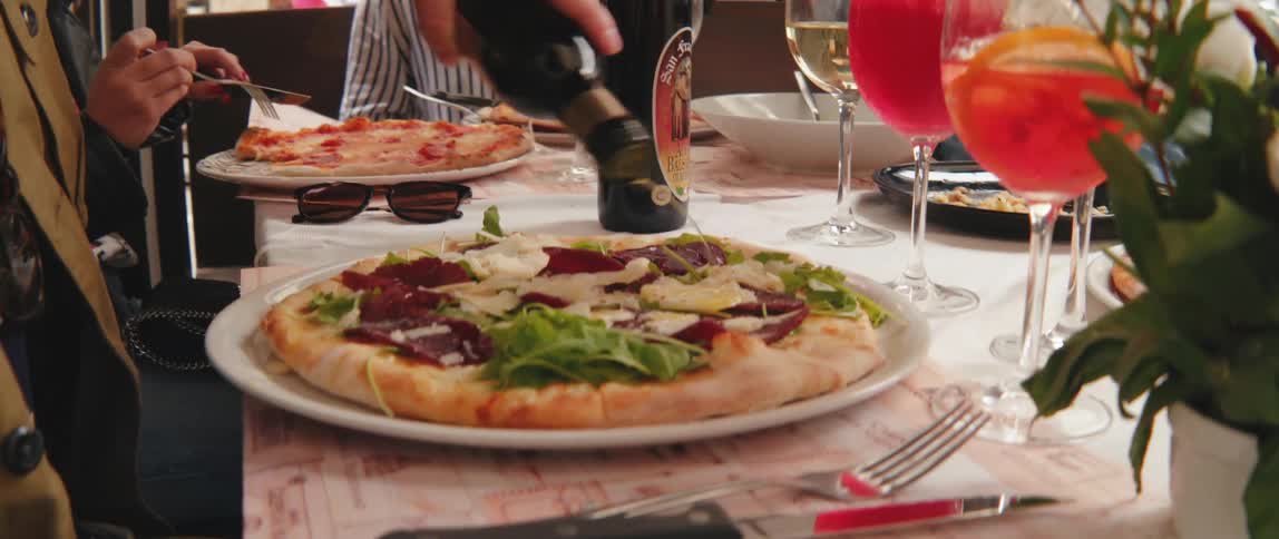 A person drizzling olive oil over a pizza in a restaurant