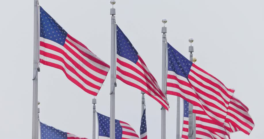 Several united states flags fly on flagpoles against a cloudy sky