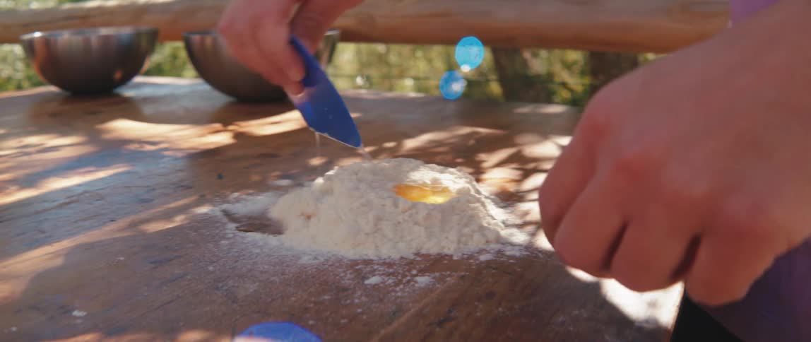 Hands of a person with a spatula adding flour with raw egg and a wooden table