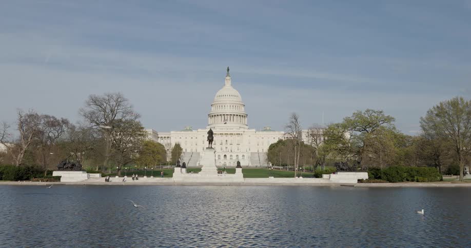 Pedestrians walk outside the us capitol building next to the reflection pool on a spring day