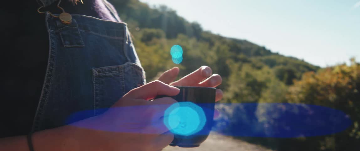 Woman hands holding a cup that emits smoke and an outdoor environment with trees around