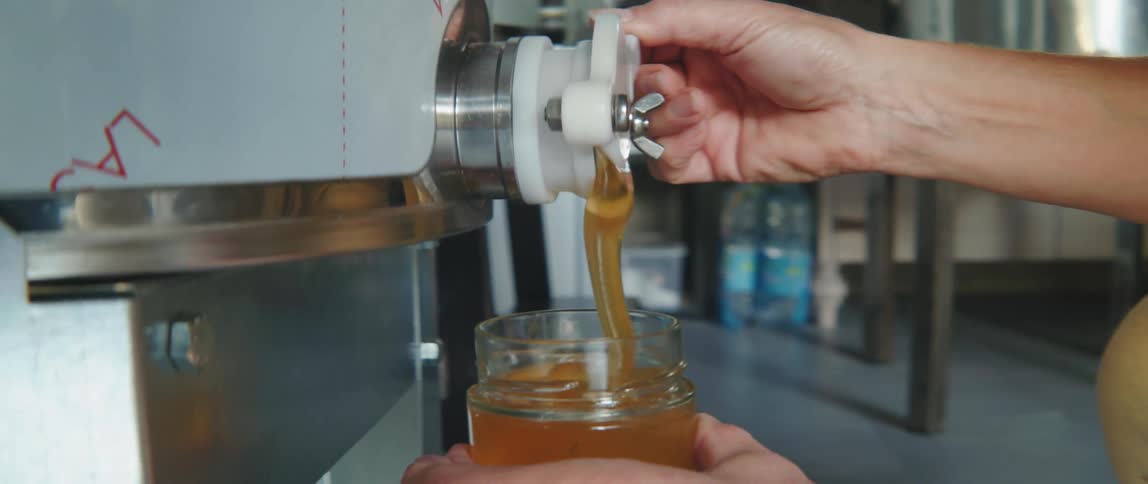 Woman hand turning a lever and pouring honey into a glass container