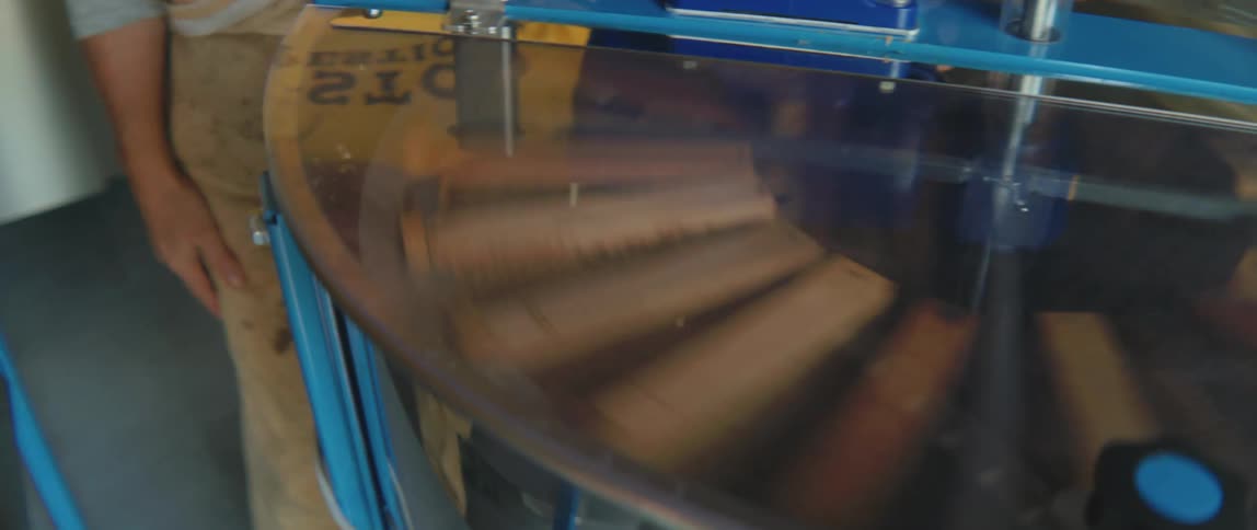 A worker in overalls stands next to a spinning machine beehive