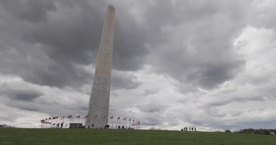 The washington monument under a cloudy sky surrounded by a circle of flags