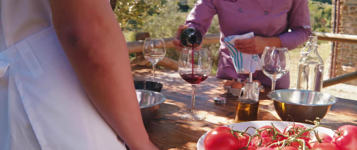 Woman pouring wine into a glass on a wooden table outdoors