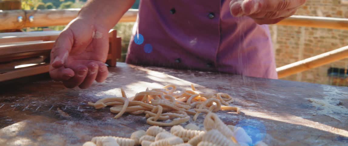 A persons hands preparing fresh pasta dough on a floured surface outdoors