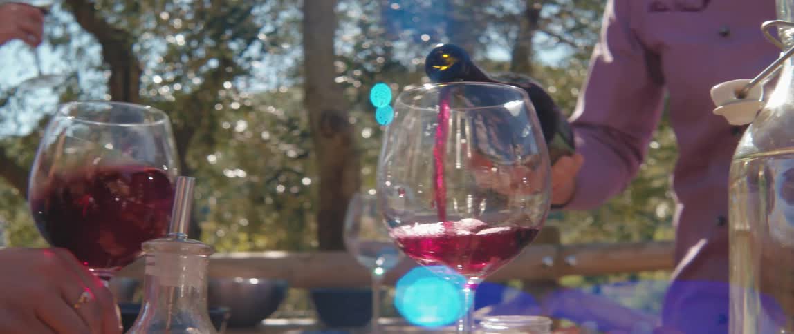 A person pours wine into a glass as others swish wine in glasses