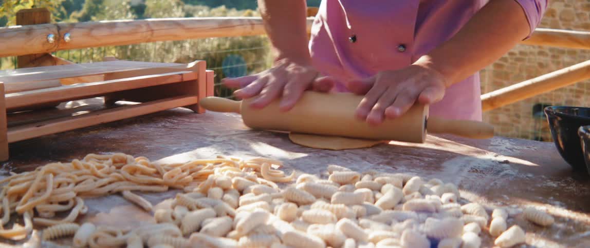 A person rolling out dough on a wooden board with a rolling pin