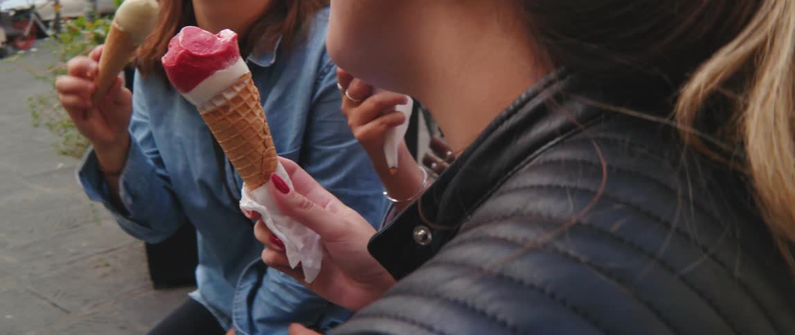 Young women sitting on a bench in a square eating ice cream
