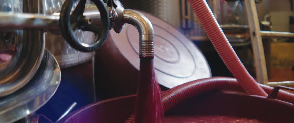Pipe pouring red liquid into a large bucket in a factory