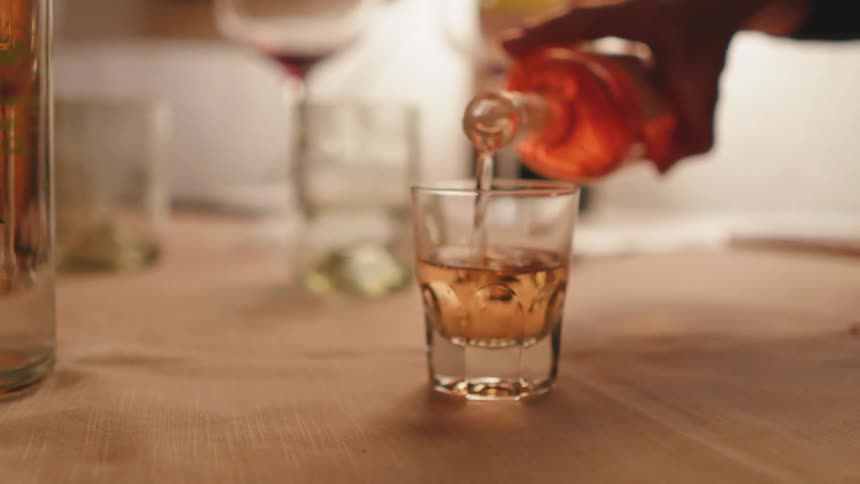 Hand pouring an alcoholic drink into a glass cup