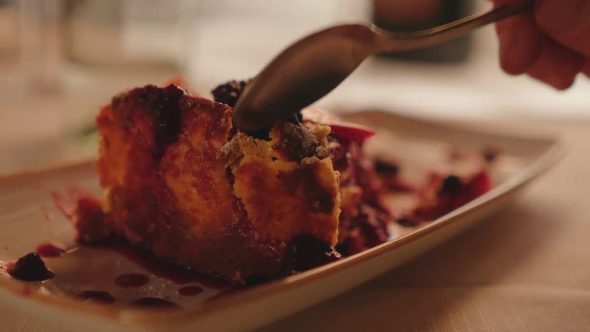 Closeup of a persons hand picking up a piece of raspberry cake with a spoon