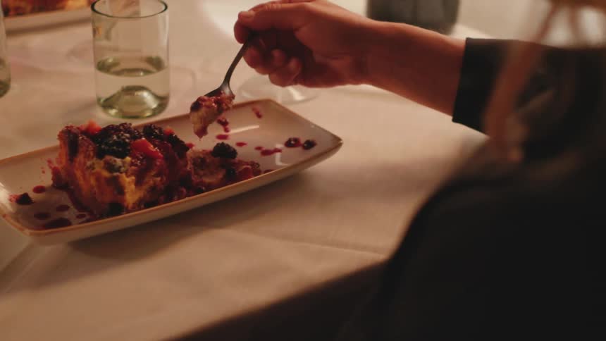 Woman sitting at the table eating a dessert cake with a spoon