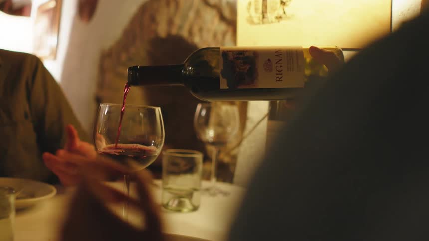 Person pouring wine into a crystal glass on a table with people around