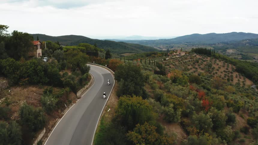 Winding road with motorcycles traveling through a rural landscape with diverse vegetation and mountains on the horizon