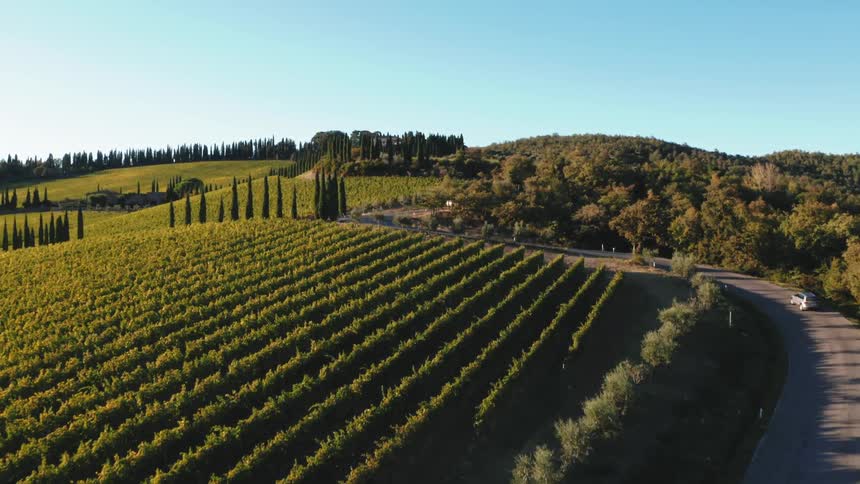 Aerial panorama of a winding street with a car and rural areas around it on a blue sky morning in Tuscany