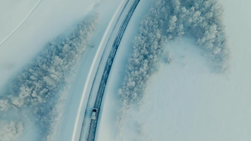 Topdown aerial view of a car driving on a road in a snowy landscape