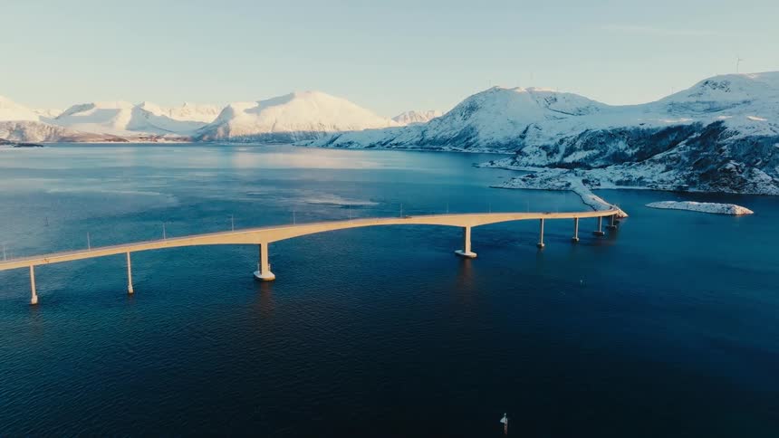 Aerial view of a bridge over a sea surrounded by icecovered mountain ranges