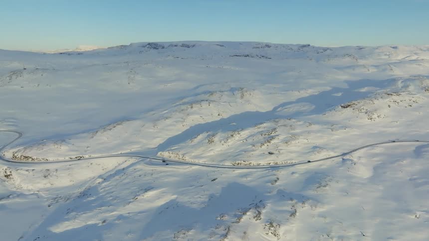 Aerial of moving cars on a road with snows on both sides on a sunny day