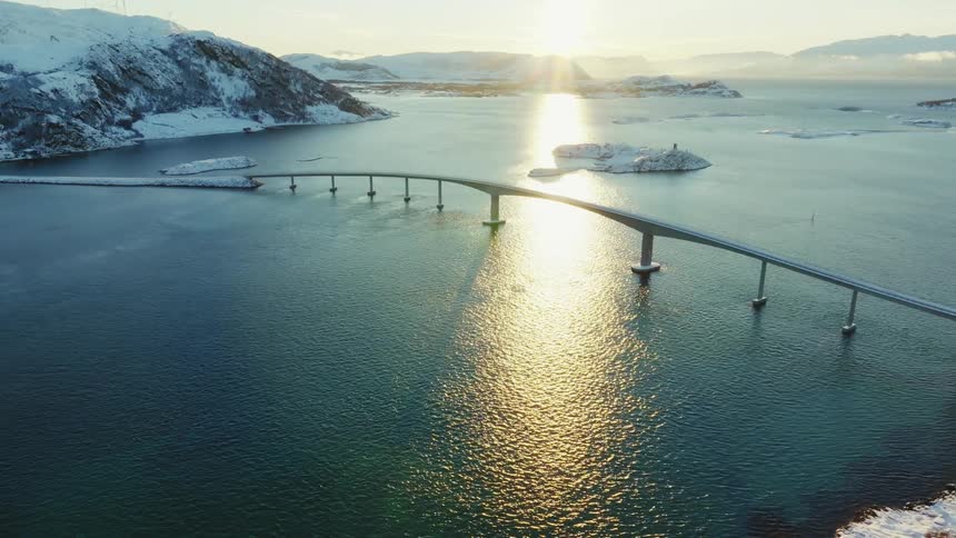 Sun shines across snowy landscape and bridge in winter