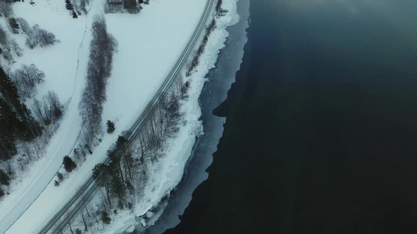 Aerial shot of a car driving on snowy road near the sea