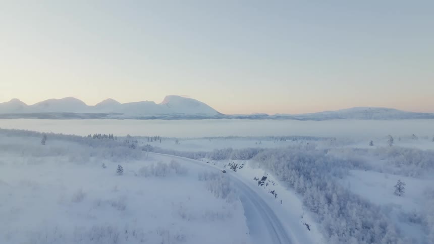 Aerial view of a car driving on a snowy road with a mountainous landscape in the background