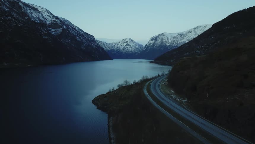 Aerial of a highway near lake with snowy mountain range in the background