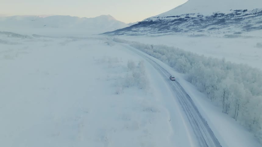 Aerial of car driving on snowy road near a snowy field